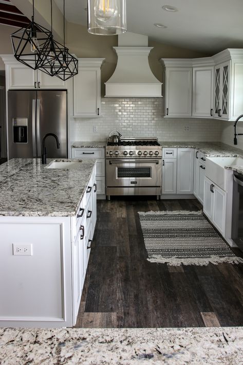 Beautifully elegant white kitchen with gray and black mottled granite and island countertops. The darker wood of the floor really makes the white cabinets, backsplash and countertops stand out. White Granite With White Cabinets, Black And White Kitchen Makeover, Kitchen Flooring With White Cabinets And Black Countertops, White Kitchen Cabinets With Gray Floors, White Cabinets And Countertops Kitchen, White Kitchen Cabinets With Darker Countertops, White Cabinets With Countertops, Gray And Black Granite Countertops, White Gray Countertops Kitchen