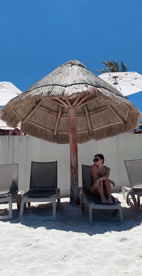 photo of clear blue sky, natural straw beach umbrella with beach chairs in a row horizontally, and white sand; young woman with black hair sits on each chair with her legs bent and arms crossed over legs; she looks to the left; she wears black sunglasses and white bikini Beach Chair Pictures, Sitting Poses Instagram, Beach Chair Poses, Cancun Outfits Vacation, Umbrella Aesthetic, Chair Poses, Cancun Outfits, Mexico Pictures, Beach Photo Inspiration