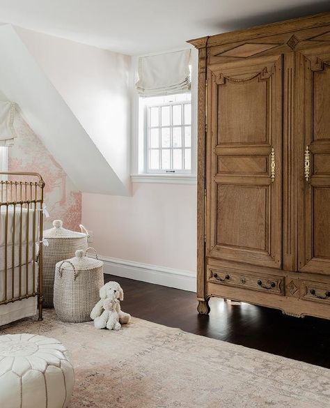 Pink French girl's nursery features a French armoire accented with antique brass hardware and placed on a dark stained wood floor beside a window covered in an off-white roman shade. French Country Baby Nursery Ideas, Dark Wood Nursery, Crib With Storage, Dark Stained Wood Floors, Pink Nursery Wallpaper, Transitional Nursery, Pink Crib Sheets, Erin Gates Design, Bear Mobile