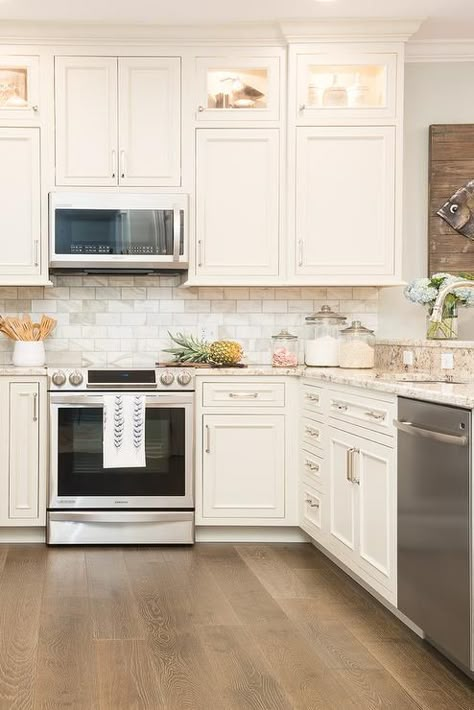 White u-shaped kitchen boasts square cabinets fitted with custom lighting and stacked above white cabinets adorning polished nickel pulls and flanking a wall mounted stainless steel microwave fixed against marble subway backsplash tiles above a stainless steel range. Off White Kitchens, Affordable Kitchen, Square Kitchen, Kitchen Cabinets Makeover, Classic Kitchen, Custom Kitchen Cabinets, Kitchen Views, Up House, Transitional Kitchen