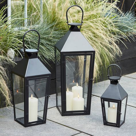 A trio of beautiful black metal garden lanterns, with realistic LED flame candles inside.With a sleek trapeze shape and large handle, style this trio together for a real statement in your garden. Our large lantern features a trio of realistic candles within and the regular and medium sizes feature a single LED candle for a warm ambience each evening. Pop 2 x C batteries (not included) into the base of each candle and opt for the 6 hour timer for automatic illumination each evening.Black metal la Black Lantern Decor, Realistic Candles, Garden Lantern, Large Lanterns, Black Lantern, Candle Base, Garden Lanterns, Black Garden, Outdoor Candles