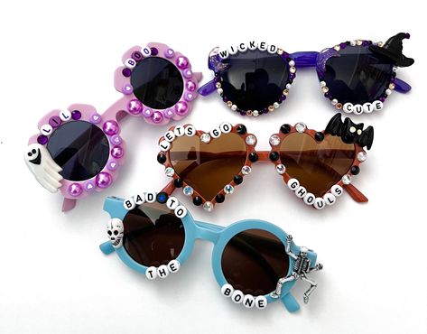 "HALLOWEEN SUNNIES!! These are so adorable-- Each pair is handcrafted by me. Using various beads, Charms, Rhinestones, and fun details!  *4 options available-- Choose your style:  1. BAD TO THE BONE 2. LETS GO GHOULS  3. WICKED CUTE 4. LIL BOO * Anti-Glare * UV Protection (UVA & UVB) * Durable and shatterproof  * They open and close smoothly  * Each item is made to order and will be ready to ship in 5-7 business days! If you need your order sooner. Please check out my \"RUSH ORDER OPTION\".  https://www.etsy.com/EyeCandyandFluff/listing/1286351273/rush-my-order-please *SHOP DISCLAIMER/WAIVER!  * Do NOT let your child put the sunglasses in their mouth as beads can become detached.    Always monitor and supervise while children are wearing these. The shop assumes no responsibility for sungla Fun Handmade Sunglasses As A Gift, Fun Handmade Sunglasses For Party, Fun Handmade Sunglasses For Parties, Fun Handmade Plastic Sunglasses, Handmade Fun Plastic Sunglasses, Handmade Plastic Fun Sunglasses, Halloween Sunnies, Halloween Sunglasses, Lets Go Ghouls