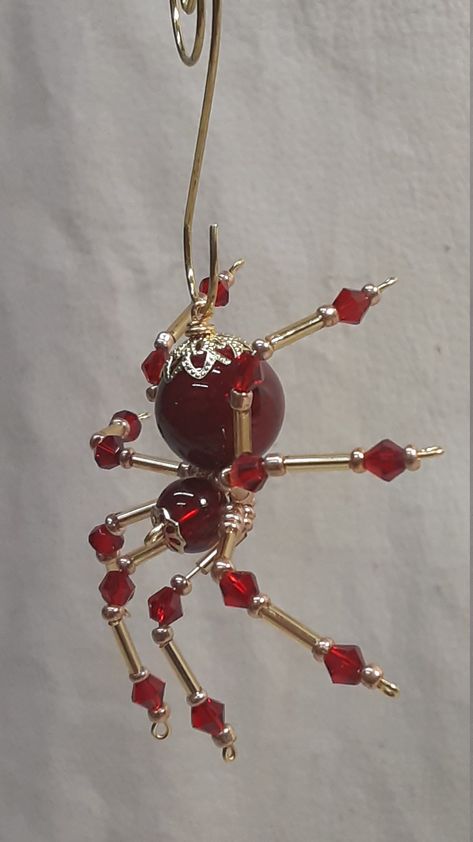 "This is a handmade beaded crystalline spider. The abdominal area is made from a red plastic bead and the head from a smaller red faceted bead. The legs are made form 21 ga. brass wire which are covered with small Red Swarovski Glass and gold glass beads that can be carefully adjusted to almost any position. Gold bead caps are also incorporated into the body. A gold decorative hook is attached to the back of the abdomen and can be used to hang the spider or be removed. The spider can be used as Wire Beaded Spider, Spider Beads, Bead Spider, Bead Spiders, Beaded Spiders How To Make, Wire Beading, Red Beads, Beaded Spider Web, Beaded Bugs