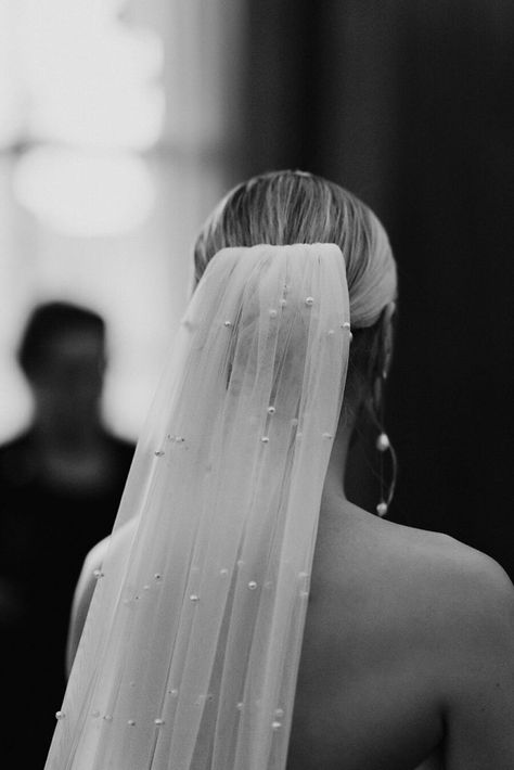 A bride wears a white strapless minimal wedding gown with a sweetheart neckline. Her blonde hair is tied in a low bun over which a long pearl veil is worn. She holds a large bouquet of fluffy white roses. Veil Low Bun, Low Bun Wedding Hair With Veil, Black Tie Aesthetic, Bride Bun, Blonde Bun, Tower Cake, Large Bouquet, Pearl Veil, Decker Bus