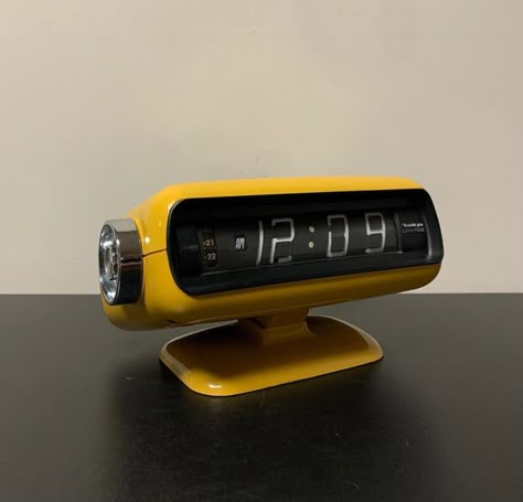 Iconic space age alarm clock manufactured by  Sankyo in the 70s. This model feature a shell with typical rounded edges made of ultra thick plastic, that has an incredible and charming yellow glossy finish. The space age allure is enhanced by the amazing and original clockwork, made of big cylinders with printed digit parts that indicate the hours and minutes. A delicate ticking add an acoustic element to the sensorial experience of this beautiful clock. Japan 70s, Flip Alarm Clock, Alarm Clock Design, Retro Alarm Clock, Vintage Alarm Clocks, Retro Gadgets, Vintage Shelf, Cool Clocks, Love Is Not