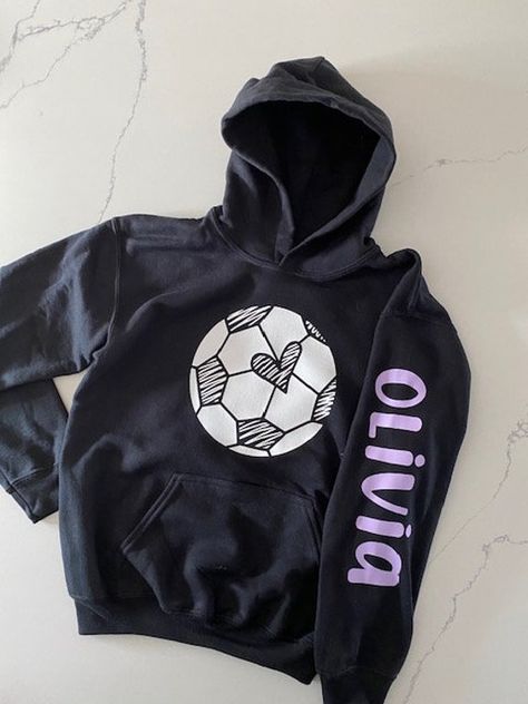 Soccer hoodie for girls with a fun design on the front.  Personalize this soccer hoodie with a name on the sleeve.  The soccer ball design includes a heart in the middle with sketch-like font.   This is a pullover hoodie with hand pocket in the front.  There are no drawstrings on this hoodie. Personalize with name in color of your choosing.  Youth Sizing:  S=6/6x, M=7/8, L=10/12, XL=14/16.  Adult sizes available only upon request. Washing Instructions: 1.  Turn garment inside out 2.  Machine was Customizable Sporty Hoodie For Game Day, Football Season Fan Merchandise Long Sleeve Hoodie, Black School Spirit Hoodie With Team Name, Fan Merchandise Long Sleeve Hoodie For Football Season, Long Sleeve Hoodie With Letter Print For Football Season, Sporty Long Sleeve Hoodie With Team Name, Sporty Hooded Hoodie For Football Season, Sporty Hoodie Sweatshirt For School, Hooded Football Season Sweatshirt