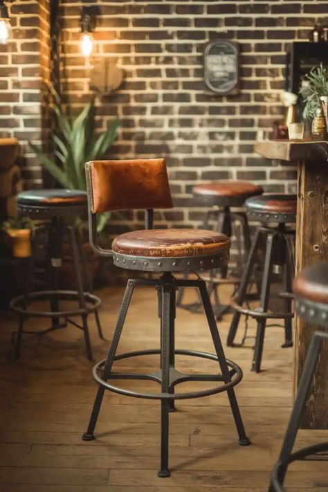 Rustic bar stool with leather seat and backrest in a cozy, dimly lit pub with brick walls and warm lighting. Industrial Restaurant Furniture, Rustic Leather Bar Stools, Bar Stools Industrial, Bar Seats Ideas, Rustic Barstools In Kitchen, Rustic Bar Stools With Back, Modern Bar Counter Design, Unique Barstools, Rustic Barstools