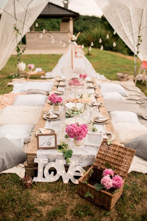 a neutral boho picnic setting with a low pallet table, neutral textiles, pink blooms, a LOVE sign and string lights over the table