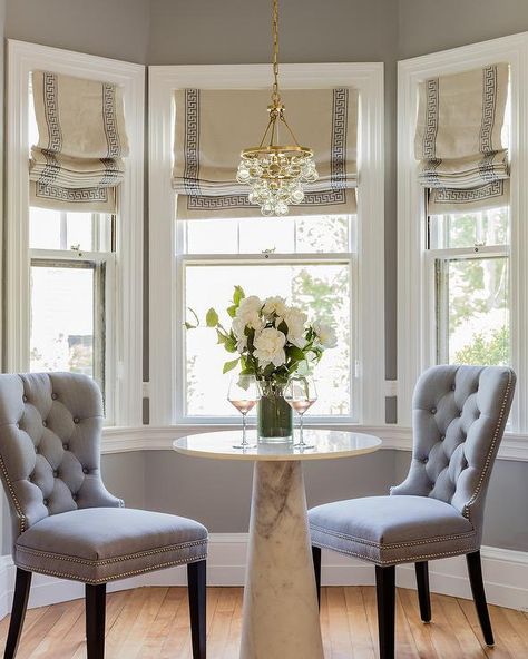 Small kitchen bay window gorgeously displays a round marble pedestal dining table paired with gray tufted nailhead dining chairs under a Robert Abbey Mini Bling Chandelier. Bay Window Roman Shades, Bay Window Decor, Bay Window Design, Bay Window Treatments, Bay Window Living Room, Kitchen Bay Window, Breakfast Nook Table, Bay Window Seat, Bay Window Curtains