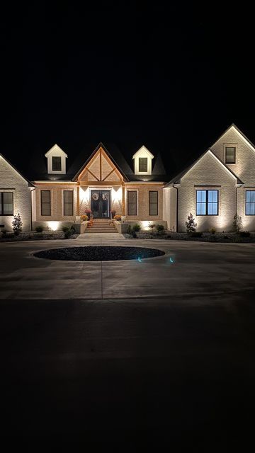 Nikki • Modern Farmhouse on Instagram: "This is one of my favorite upgrades we made. I absolutely love the look of our house at night. It’s all connected to a timer set to automatically come on at dusk until dawn. Is this something you have considered for your home? #frombuildtobuilt #uplighting #premierlandscape #customhomes #homeswithpurpose #whitebrick #landscapelighting #ourbuildjourney #housebuildingtips" Home Exterior Lighting At Night, Lights On Front Of House, Exterior Up Lighting On House At Night, Ranch House Outdoor Lighting, House Landscape Lighting, Exterior Uplighting House, House Uplighting Outdoor, Lights For Outside House, Lights On House Exterior At Night