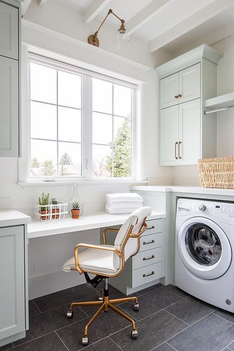 Multi-purpose space brings together a laundry room and home office with stunning light gray cabinets, a white floating desk and slate floor tiles. White Floating Desk, Laundry Craft Rooms, Laundry Room Countertop, Grey Laundry Rooms, Slate Floor, White Laundry Rooms, Light Gray Cabinets, Laundry Room Lighting, White Laundry