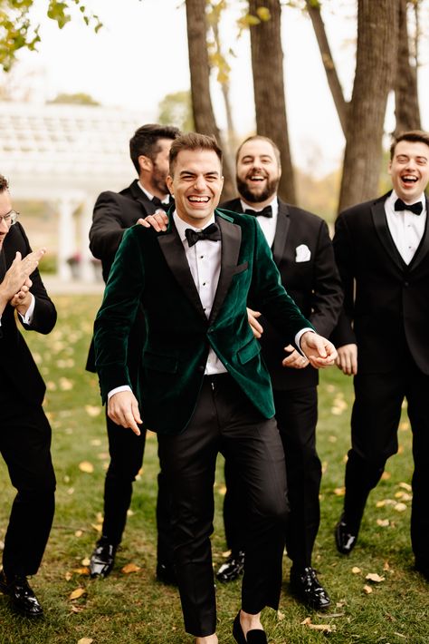 Group of groomsmen wearing black tux and groom is wearing green velvet jacket Groomsmen Velvet Jacket, Green Velvet Bridesmaid Dresses With Groomsmen, Velvet Green Tuxedo Wedding, Green Groom Suit Black Groomsmen, Black And Emerald Green Suit, Velvet Groomsmen Attire, Groom And Groomsmen Attire Green, Winter Groomsmen, Groomsmen Attire Black