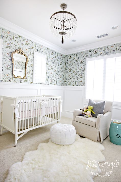 Lovely nursery features aviary wallpaper on top half of wall and wainscoting on bottom half of wall framing gilt ornate mirror over white traditional crib dressed in white and pink crib bedding. Girl's nursery with white beaded glass chandelier over oatmeal linen glider accented with gray pillow and paired with turquoise stool and white Moroccan leather pouf over sheepskin rug layered over beige wall to wall carpeting. Mcgee Design, Transitional Nursery, Nursery Window, Shea Mcgee, Bird Nursery, Baby Nurseries, Babies Room, House Of Turquoise, Nursery Room Design