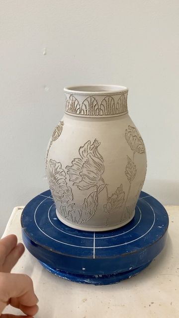 Ayla Mullen on Instagram: "I finished carving this Poppy vase today! 🌸 Tomorrow I will scrub off all the little clay bits at the edges of the carvings and inlay blue underglaze into the design. I haven't worked much with poppy designs in the past few months, and it felt good to come back to my favorite flowers. I really can't say why they're my favorite-- something about the expressiveness of every stage of bud, bloom, and seed pod captivates me endlessly. What is your favorite flower? #pop Designs To Carve Into Clay, Ceramic Flower Vase Design, Poppies On Pottery, Carved Vases Pottery, Ceramic Vase Painting Ideas Patterns, Ceramic Flower Carving, Vase Carving Ideas, Carved Flowers Pottery, Feminine Pottery