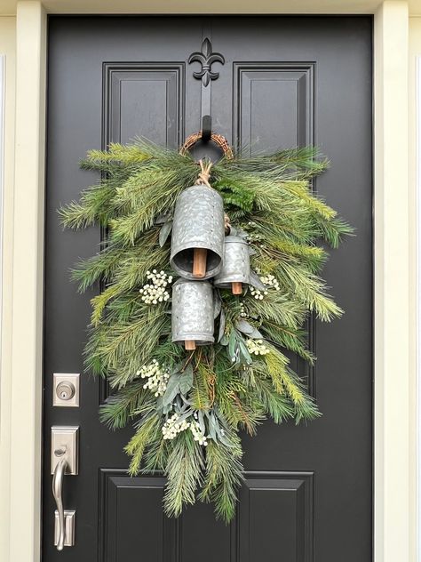 Our Silver Bells Christmas Pine Swag Wreath is the perfect combination of holiday tradition and rustic elegance. The trio of vintage metal bells adds a charming, old-world feel, while the evergreen branches and white berries create a serene winter scene. Hang it on your covered front door to bring the sound of Christmas into your home, filling the air with peace and goodwill. Christmas Wreath Display, Christmas Door Swag With Bells, Silver Bells Christmas Theme, Christmas Wreaths Front Door, Christmas Wreath Inspiration, Evergreen Wreaths For Christmas, Silver Bells Christmas Decorating Ideas, Christmas Decor Ideas For Front Porch, Christmas Wreaths For Front Door Rustic