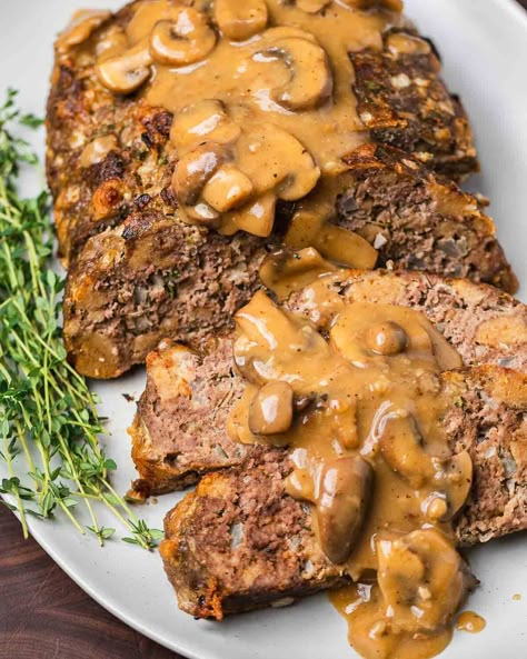 Meatloaf with brown gravy is the ultimate comfort food! The meatloaf is loaded with flavor from ground chuck, garlic, onion, parsley, and fresh thyme and topped with a hearty rib-sticking mushroom brown gravy. Perfect with a side of garlic mashed potatoes and green beans. #meatloaf #meatloafwithmushrooms #meatloafandbrowngravy #meatloafrecipes Sip And Feast Recipes, Meatloaf With Mushrooms, Brown Mushroom Gravy, Brown Gravy Meatloaf, Mushroom Meatloaf, Meatloaf With Gravy, Tasty Meatloaf Recipe, Italian Beef Stew, Brown Gravy Recipe