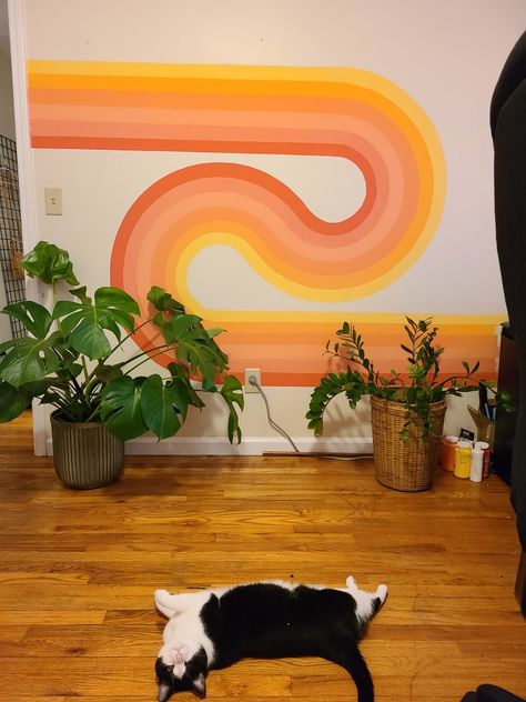 70s wavy wall art with pink peach yellow orange tones in a rainbow looping together with a big monstera plant and zz plant on the right wooden floor with a very cute black and white Cat laying on the floor looking at the camera Aesthetic Walls Painted, 70s Wall Mural Retro, Painting Ideas On Wall Aesthetic, Groovy Mural Art, Aesthetic Wall Mural Bedroom, Wall Painting Inspo Aesthetic, 70s Mural Art, Pink 70s Aesthetic Wallpaper, 70s Wall Mural Diy