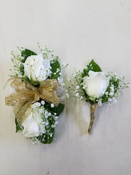 White roses, baby's breath, green leaves and gold trim wrist corsage and boutonniere. White And Green Corsage And Boutonniere, Homecoming Corsage For Green Dress, White Flower Corsage And Boutonniere, Sage Green Corsage And Boutonniere, White Green Corsage, White Rose Corsage And Boutonniere, White Corsage And Boutonniere Set, Corsage Prom White And Gold, Green And Gold Corsage Prom