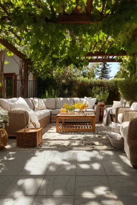 Inviting outdoor patio with wicker furniture and plush cushions under a vine-covered pergola, a wooden table with a citrus fruit centerpiece bathed in sunlight. European Outdoor Space, European Inspired Patio, Modern European Backyard, Outdoor Parisian Patio, European Backyard With Pool, Covered Patio Design, Patio Layout, Cozy Patio, Patio Inspiration