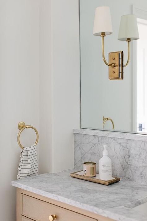 Bathroom features brass Hulton sconces on an arched vanity mirror over a tan French washstand with a gray marble countertop and backsplash and brass towel ring. Marble Countertop And Backsplash, Block Print Wallpaper, Kate Marker Interiors, Grey Floor Tiles, White Shiplap Wall, Grey Headboard, Arched Mirror, Transitional Bathroom, Gray Marble