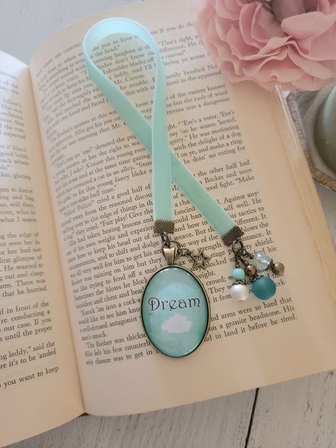 This bookmark is created with aqua velvet ribbon and a watercolor picture pendant of an cloud and the word "dream" on an aqua background. I've accented with glass bead charms and a bronze star charm. Positively dreamy! Use drop down menu to choose length of ribbon. This is the usable length of the bookmark and doesn't include the end charms. Pendant is approx. 1.25x1.75 inches. All orders are wrapped in kraft brown tissue and twine. We do offer gift message options. Please enter your gift ... Charm Bookmark, Journal Jewelry, Aqua Background, Bookmark Craft, Homemade Birthday Cards, Beaded Bookmarks, Picture Pendant, Diy Bookmarks, Book Markers