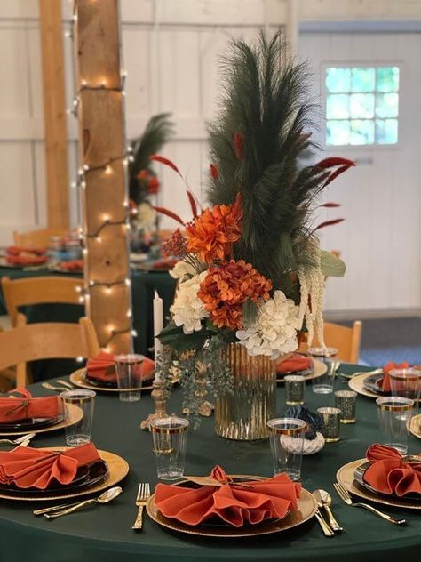 Set up beautiful tablescapes at your event using an attractive orange, green, & gold color palette. Drape the tables with emerald green tablecloths & flaunt orange & white hydrangeas & white amaranthus sprays, along with green plumes in vases. Also, set gold mercury candle holders & use gold chargers, black plates, gold cutlery, orange napkins, & gold rim clear flutes to glam up the place setting. Moreover, cover the venue pillars with string lights to enhance the ambiance. Green And Rust Wedding Table Decor, Orange Green And Gold Wedding, Emerald Green And Rust Wedding Table, Emerald Green And Burnt Orange Wedding Centerpieces, Orange Green Wedding Decor, Emerald Green Burnt Orange And Gold Wedding, Orange And Gold Wedding Theme, Emerald Green And Rust Wedding Centerpiece, Emerald Green And Burnt Orange Wedding Decor