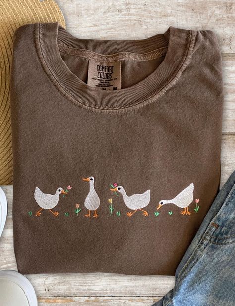 Embrace the beauty of nature and add a touch of artisanal flair to your wardrobe with our embroidered geese and tulips Comfort Colors t-shirt. Perfect for nature lovers and fashion enthusiasts alike.  Pigment dyed colors with a vintage look.  This is an adult unisex t-shirt.  CARE INSTRUCTIONS: Please turn inside out and wash in cold water with a mild detergent.  Do not use bleach.  Tumble dry low or dry flat, if possible.  Iron on low heat, if needed.  Do not use steam.    SHIPPING: All shipmen Cute Tee Shirt Outfits, Gifts For Cottage Core, Small Embroidery Designs On Tshirt, Embroidery Ideas Machine, Hand Embroidered T Shirt, Embroidery T Shirt Ideas, Tulip Clothes, Cute Etsy Finds, Cool Embroidery Ideas Clothes