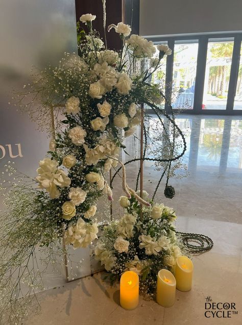 White flower decor with the candles  at the entrance for a house warming party that will elevate your whole space. Wedding Favours Muslim, White Flower Decor, Door Entrance Decor, Door Flower Decoration, Green Floral Decor, House Warming Party, Standing Flower, Party Entrance, Mehndi Decor