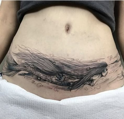 For the person who loves mermaids comes this stunning mermaid tattoo for tummy tuck scars! The mermaid is created in black ink and extends throughout the width of the stomach and onto the hip area. The mermaid’s long, flowing hair expertly hides all elements of the scar, while the bubbles and flowing water add to the final look. Lower Abdomen Tattoo, C Section Scar Tattoo, Lower Belly Tattoos, Abdomen Tattoo, Lower Stomach Tattoos, Tummy Tattoo, Tattoo Over Scar, Stomach Tattoos Women, Tattoos To Cover Scars