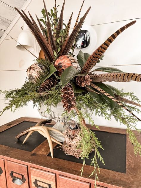 Pheasant feathers and ornament combine with pinecones and greenery for a table centerpiece. Pheasant Feather Decor, Christmas Centrepiece Ideas, Antler Centerpiece, Winter Mantel Decor, Woodland Centerpiece, Antlers Decor, Floral Antlers, Greenery Centerpiece, Feather Centerpieces