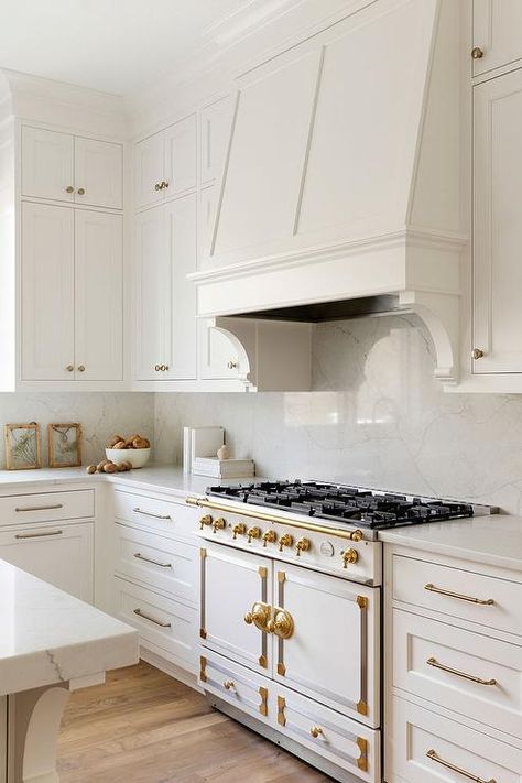 Kitchen features a white and gold La Cornue CornuFé 110 Range and a white wooden range hood with corbels and honed marble slab backsplash and white cabinets with brass pulls. Contemporary Kitchen Hardware, Studio Mcgee Kitchen Hardware, Studio Mcgee Sunset House, Custom Hoods For Kitchen, Modern Hood Vent, Hood Cabinet, Mcgee Kitchen, Studio Mcgee Kitchen, Kitchen Dining Nook