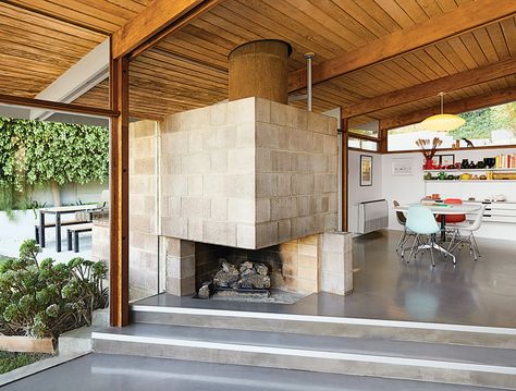 The dining area features a distinctive cinder block fireplace. Molded plastic side chairs are arranged around a Segmented Base table, all by Charles and Ray Eames for Herman Miller. The space is illuminated by a Saucer pendant lamp by George Nelson from Modernica.