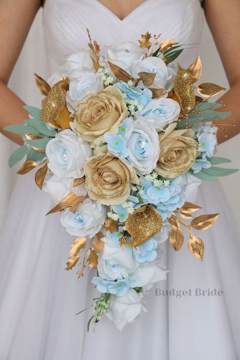 This lovely assortment of light blue roses with jewel centers and gold glitter tipped roses is bound to turn heads on your wedding day. This lovely cascading brides’ bouquet from the is an absolutely breathtaking arrangement for any bride to be, in any season. Sage greenery and gold glitter calla lily accents complete the look and add a delicate realism to this beautiful bouquet. This bouquet is 10” wide, 18” long, and is crafted by our in-house florists without using a foam base to anchor the f Cyan And Gold Wedding Theme, Blue And Gold Flower Arrangements, Blue And Gold Wedding Flowers, Light Blue And Gold Wedding Theme, Sky Blue And Gold Wedding, Gold And Light Blue Wedding, Tiffany Blue And Gold Wedding, Light Blue Gold Wedding, Light Blue And Gold Wedding