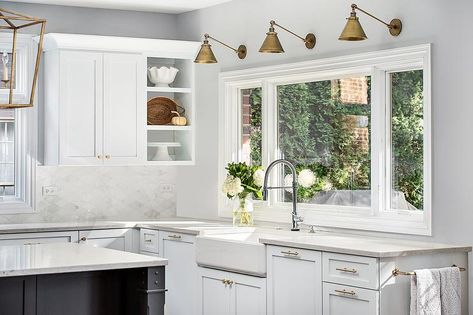 Three antique brass swing arm sconces are fitted to a light gray wall above a window positioned over a farmhouse sink paired with a polished nickel gooseneck faucet. Lighting Over Kitchen Sink, Over Kitchen Sink Lighting, Kitchen Sconces, Small Kitchen Lighting, Over Kitchen Sink, Kitchen Sink Lighting, Above Kitchen Sink, Window Over Sink, Kitchen Sink Window