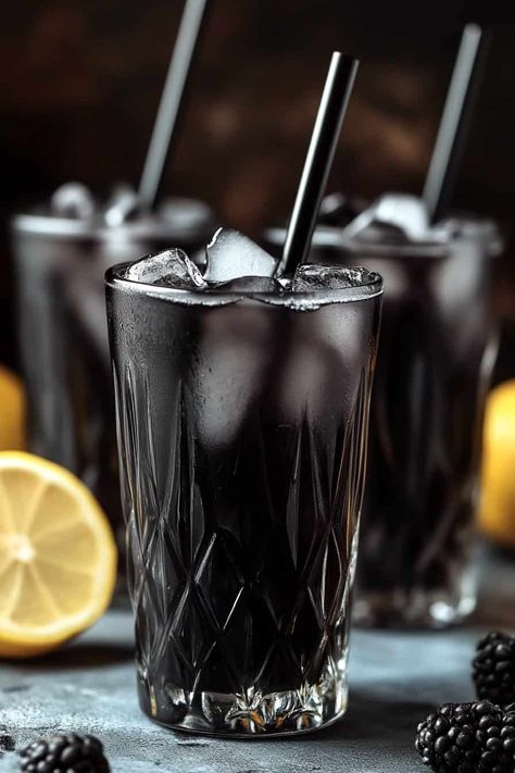 Three glasses of Black Charcoal Lemonade with black straws and ice cubes, garnished with blackberries, with lemon halves in the background. Bartending Drinks, Charcoal Lemonade, Pineapple Lemonade Punch, Halloween Themed Desserts, Blue Hawaiian Punch, Halloween Themed Snacks, Peach Margarita, Spooky Halloween Food, Lemonade Punch