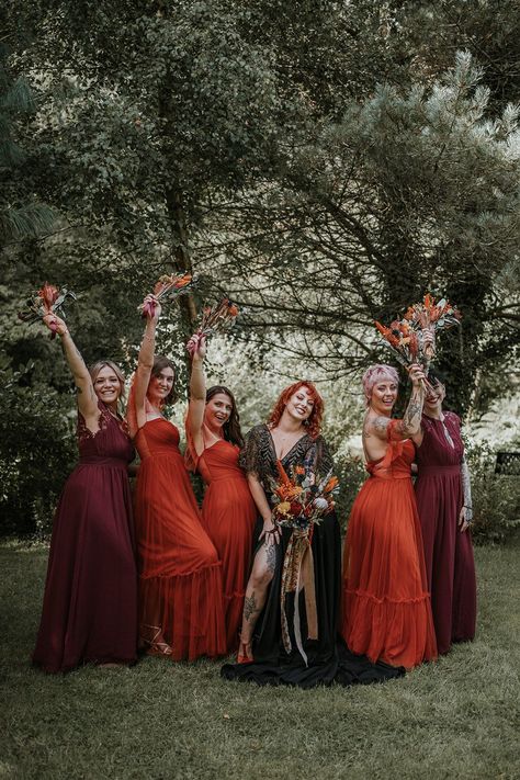 Bride in black dress for wedding in Devon standing with bridesmaids in mismatched burgundy and burnt orange bridesmaid dresses holding burnt orange dried flower bouquets | Katy Jones Photography Black Wedding Dress Orange Bridesmaids, Burnt Orange Burgundy Black Wedding, Black Burgundy And Burnt Orange Wedding, Burnt Orange Black Wedding, Witch Bridesmaid, Burnt Orange Bridal Party, Mismatched Burgundy Bridesmaid Dresses, Orange And Burgundy Wedding, Halloween Bridesmaid Dress