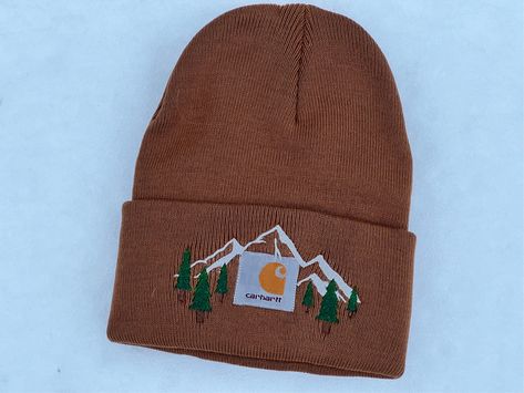 Adult Embroidered Forest And Mountain Carhartt Knit Cuffed Beanies. This hat is the perfect gift for that special someone who loves to stand out from the crowd. Whether you're hitting the slopes, working outdoors, or just strutting around town, this beanie is sure to turn heads and keep you cozy. With its unique embroidery, this winter essential is a must-have!  The Carhartt brand is well known for its durability and quality, and this beanie is no exception. Made with high-quality materials, it's designed to withstand the toughest winter weather conditions. The embroidered floral design adds a touch of personality and style to the classic Carhartt look. This beanie is not just a winter accessory; it's a statement piece that will last for years to come.  Sizing: One Size Fits Most Materials Winter Hat Embroidery Ideas, Hand Embroidery Carhartt Beanie, Manly Embroidery, Embroidered Carhartt Hat, Embroidery Carhartt Beanie, Carhartt Hat Embroidery, Embroidery On Beanie, Beanie Embroidery Ideas, Carhartt Beanie Embroidery