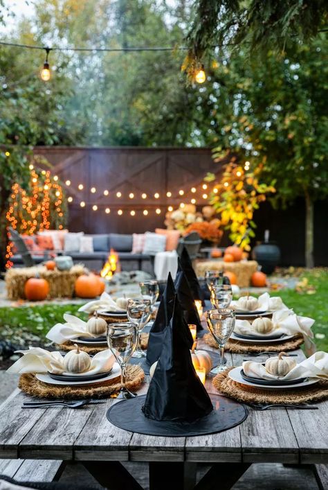 Turn your yard into a pumpkin patch by surrounding your seating area with string lights, pumpkins, and hale bales. Then, set an outdoor table with a mini white pumpkin at each place setting, and witch hats running down the center of the table. #fallaesthetic #fallbackyardparty #fallcenterpiece #pumpkindecor  #falldecor #bhg White Pumpkin Centerpieces, White Pumpkin Decor, Halloween Tablescape, Porch Pumpkins, Halloween Party Dinner, Pumpkin Display, Creepy Halloween Decorations, Halloween Dinner, Pumpkin Centerpieces