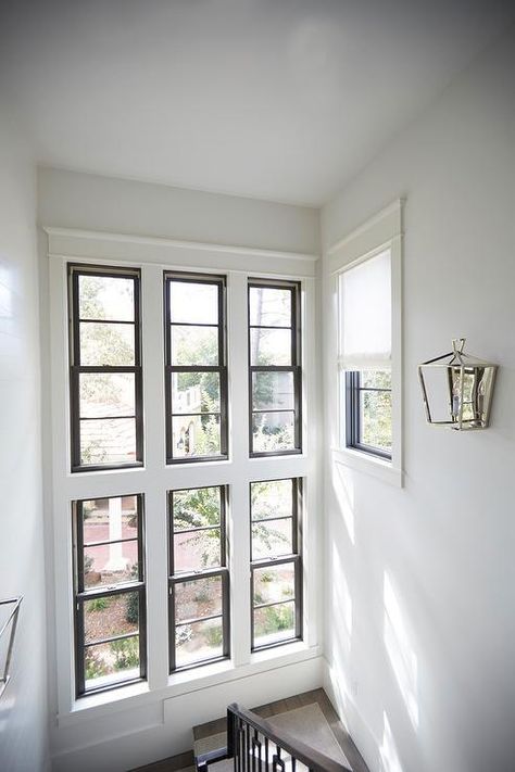 A stained wood staircase landing covered in a beige runner is lit by chrome sconces and positioned beneath stacked windows. Window Near Staircase, Stair Case Windows, Duplex Staircase Window Design, Staircase Landing Window Design, Window In Stairs, Stairs Window Design From Outside, Staircase Window Design Exterior, Staircase Window Design Modern, Window In Staircase