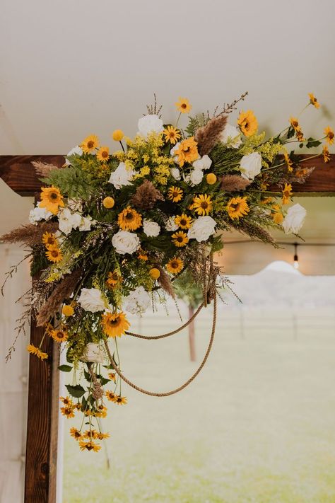 A wooden ceremony arch for a western wedding include cowboy ropes along with flowers in white and yellow including sunflowers, white roses, solidago, craspedia, ferns, small pampas for an august wedding in wyoming. Created by destination wedding florist whirly girl flowers from sheridan wyoming. White and yellow wedding inspiration. Sunflower wedding, Not Tacky Sunflowers And White Roses, Western Wedding Ceremony, Wedding Ceremony Arbor, Ceremony Arbor, Wooden Wedding Arches, Sunflower Wedding Decorations, Sunflowers And Roses, Sunflower Arrangements, Sunflower Themed Wedding