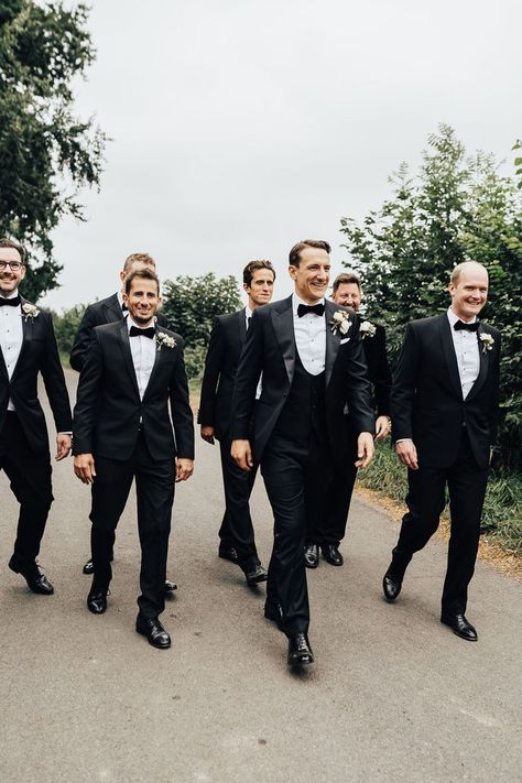 Groom and groomsmen in black tie and floral buttonholes walk down road. Black Tie Groom And Groomsmen, Wedding In Garden, Green Satin Bridesmaid, Groomsmen Attire Black, Groom Attire Black, Green Satin Bridesmaid Dresses, Sperry Tent Wedding, Black Tie Wedding Guest, Sperry Tent