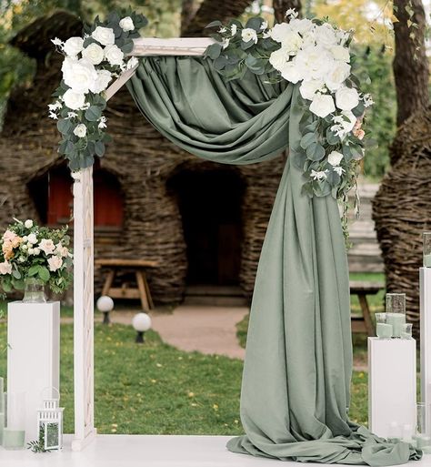 White wood rectangle wedding arch  with white rose and eucalyptus flower swag on each top corner. Eucalyptus color fabric draped from top middle to top right and flowing down right side of arch. Eucalyptus Ceremony Arch, Eucalyptus And Cream Wedding, Arch Spray Wedding, Olive Green Wedding Arch, Outside Gazebo Wedding Ideas, Simple Green And White Wedding Decor, Eucalyptus Wedding Backdrop, Gazebo Decorating Ideas Wedding Simple, White Rose Themed Wedding