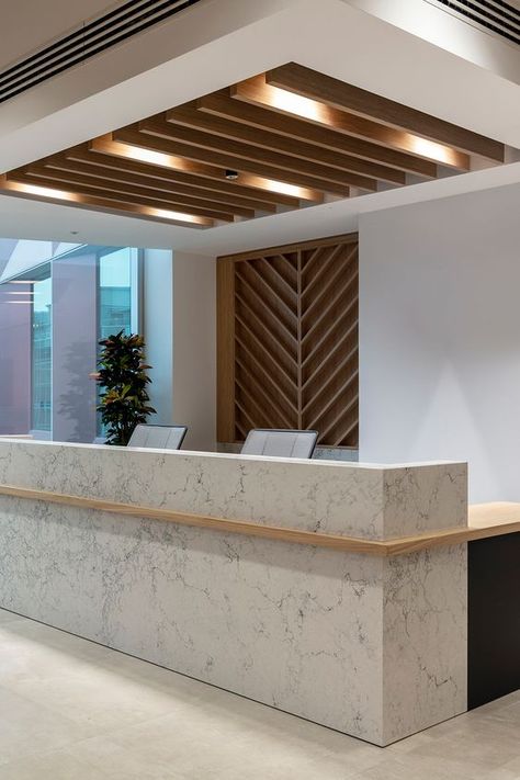 An office recpetion desk with marble used as a hard wearing and high quality frontage and an oak worktop mirroring the timber feature ceiling above. Office Ceiling Design Modern, Reception Office Ideas, Reception Ceiling Design, Office Reception Desk Designs, Marble Reception Desk, Unique Reception Desks, Office Reception Counters, Office Ceiling Design, Modern Reception Desk Design