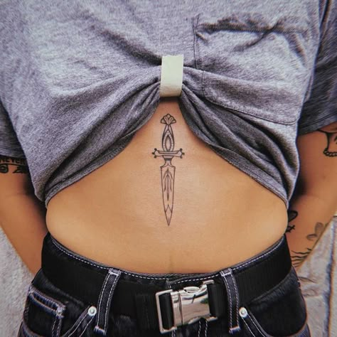 Tiny stomach dagger by Belladona Hurricane Sternum Knife Tattoo, Women Sternum Tattoo Ideas, Tattoo Between Breast Women, Dagger Sternum Tattoo Women, Athame Tattoo, Dagger Chest Tattoo Female, Dagger Sternum Tattoo, Tattoos Between Breast, Related Tattoos