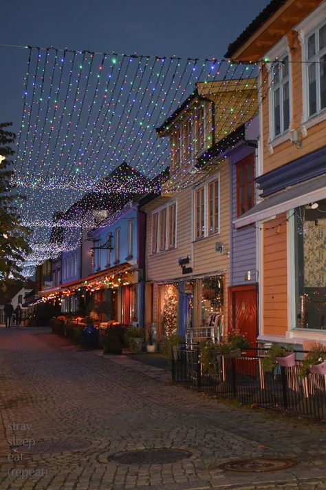 Twinkle lights shimmer over a cobblestone walkway lined with colorfully painted buildings. Norway City, Norway House, Stavanger Norway, Norway Travel, Colourful Buildings, Stavanger, Dream Holiday, Stockholm Sweden, White Houses