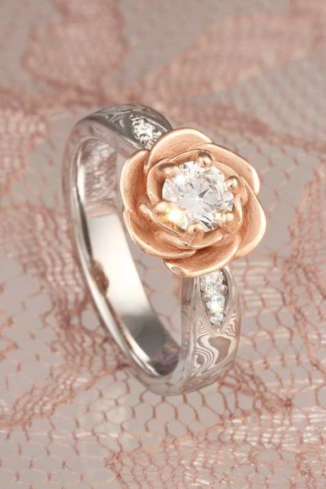 A blossoming rose cradles the center diamond or sapphire in this floral engagement ring. The rose is planted on a band of mokume gane, with 0.09 ctw diamond accents in leave-shaped recesses. This design is a great choice for modest-sized center stones, but can also be scaled up for larger stones. Rose Shaped Engagement Ring, Flower Setting, Gothic Engagement Ring, Floral Engagement Ring, Engagement Ring Inspiration, Mokume Gane, Flower Engagement Ring, Gold Diamond Wedding Band, Classic Engagement Rings