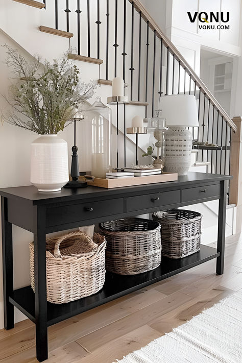 A stylish console table setup in an entryway featuring a black console table with woven baskets underneath, elegant decor items like vases and candles, and a modern staircase in the background. Black Console Table Decor, Black Entryway Table, Console Table Entryway, Console Entryway, Console Table Styling, Black Console Table, Console Table Design, Console Table Decorating, Entryway Table Decor