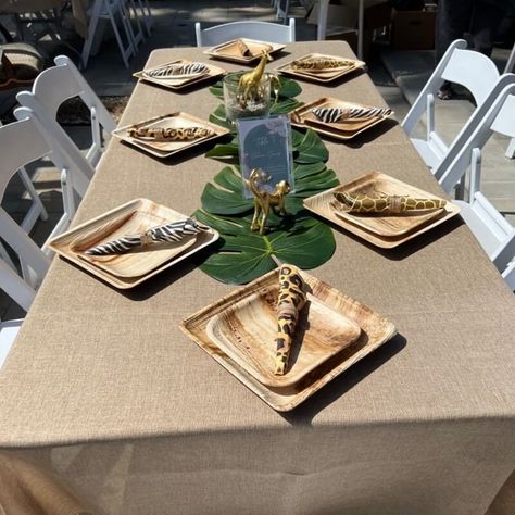 Ooze earthy elegance into your outdoor jungle themed party by setting up nature-inspired tablescapes and feel the freshness in the air. Dress up the tables in a natural burlap tablecloth and arrange white resin folding chairs for a comfortable seating. Make your tabletops feel more inviting by arranging Monstera leaves in the middle and place number sign holder & animal centerpieces, also, arrange birch wood square plates and tiger print napkins to make your place settings an outstanding one. Themed Table Settings, Animal Centerpieces, Jungle Themed Party, Event Decor Ideas, Air Dress, Party Decorations Table, Burlap Tablecloth, Earthy Elegance, Monstera Leaves