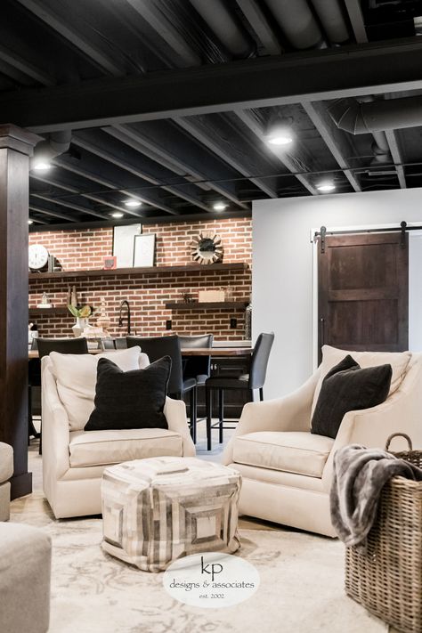 The client wanted to trade out their unfinished basement for a casual hangout where they could entertain and connect. The design inspiration was industrial with a touch of traditional to tie into the upstairs aesthetic. The entire lower level was renovated, adding a bedroom, bathroom, bar, and TV projector room. The finishes include traditional wainscotting and sconces in the TV area, an exposed ceiling, cold wine storage under the stairs... Basement Storage Closet Ideas, Upstairs Aesthetic, Black Basement Ceiling, Projector Room, Exposed Basement Ceiling, Cheap Basement Remodel, Industrial Basement, Low Ceiling Basement, Exposed Ceiling