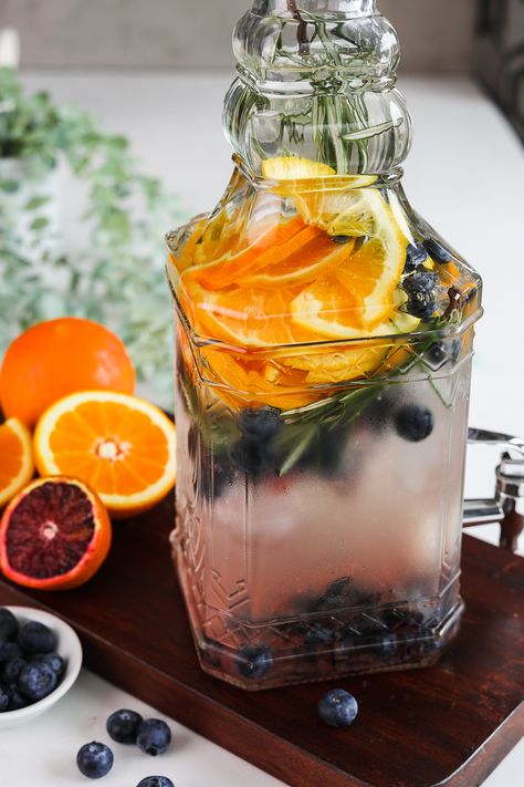 This Summer easy DIY flavored water infusion is flavoured with blueberries, fresh orange slices and sprigs of rosemary to create a refreshing summer drink! Learn how to make orange water infusion in this blog post. Fancy Water For Party, Fall Fruit Water, Orange Water Recipe, Thanksgiving Infused Water, Flavored Water Recipes Party, Thanksgiving Fruit Infused Water, Healthy Flavoured Water, Fall Flavored Water, Citrus Water Recipe For Party